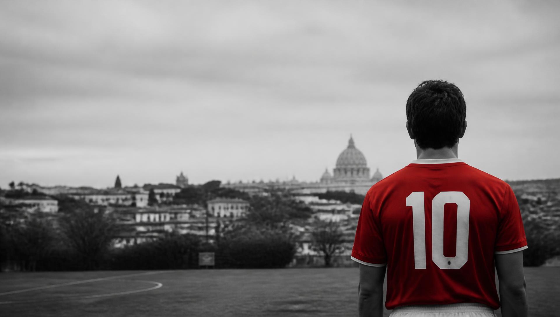 Giovane calciatore con maglia rossa di spalle su un campo a Roma
